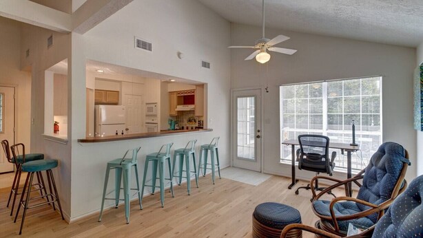 A modern kitchen with bar stools, a dining area with chairs, and a large window with blinds.