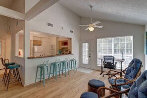 A modern kitchen with bar stools, a dining area with chairs, and a large window with blinds. - Perfect for Business Professionals (Tomball)