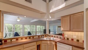 A kitchen with wooden cabinets, a dishwasher, and a large window with a view of trees.