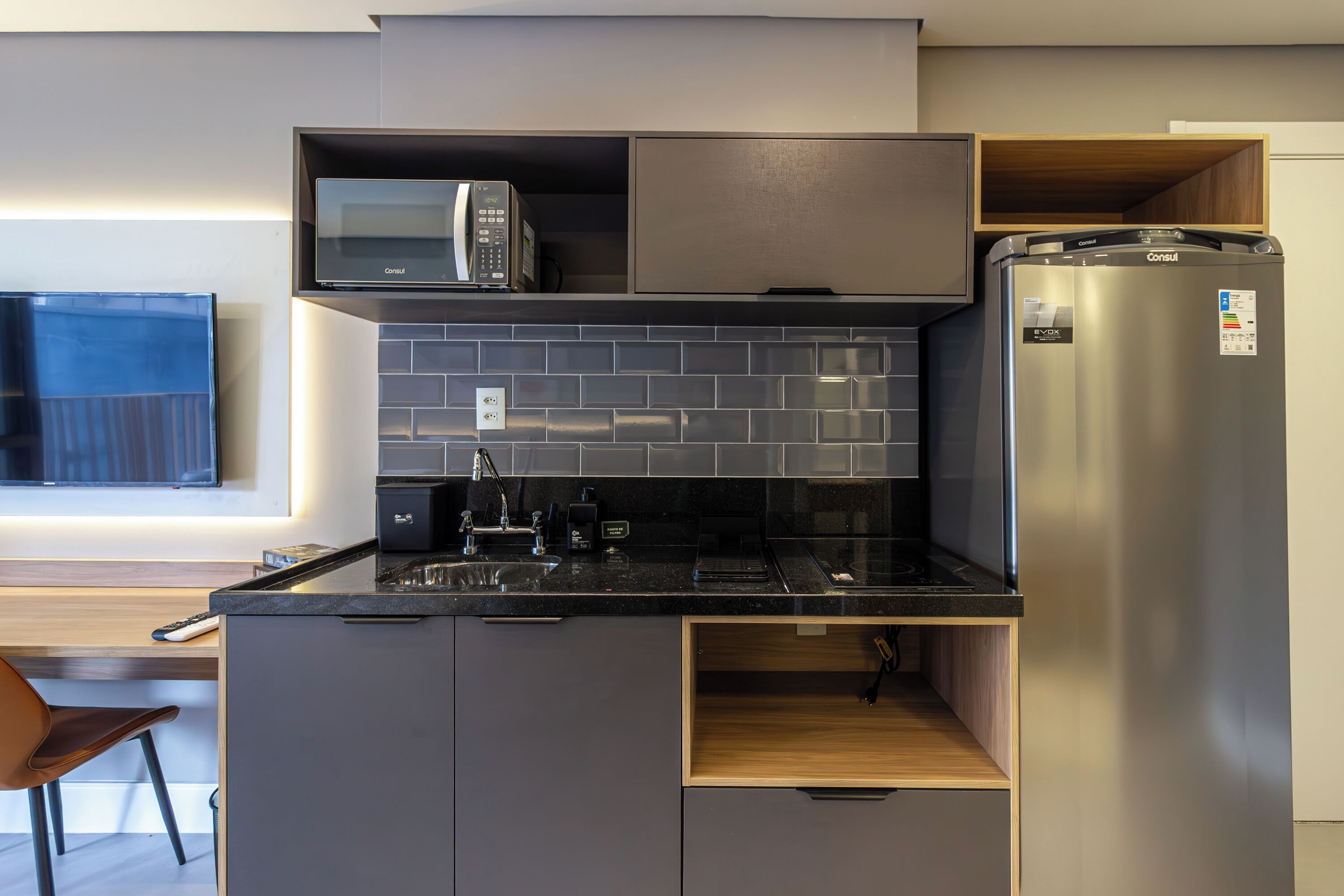 Una cocina moderna con microondas integrado, refrigerador de acero inoxidable y encimera de madera.