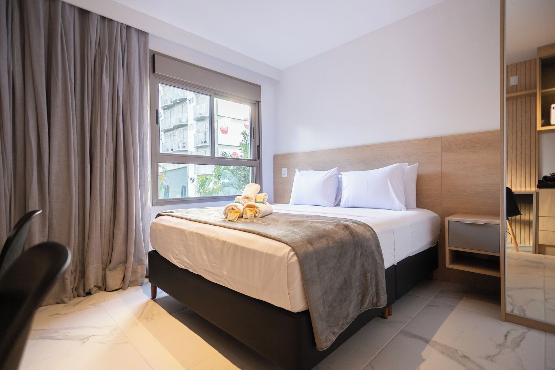 A hotel room with a bed, a chair, a wardrobe, and a window with curtains.
