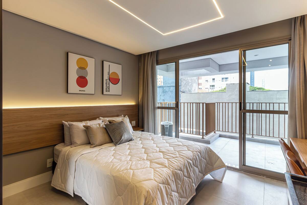 A modern bedroom with a large bed, a view of the city through a sliding glass door, and artwork on the wall.