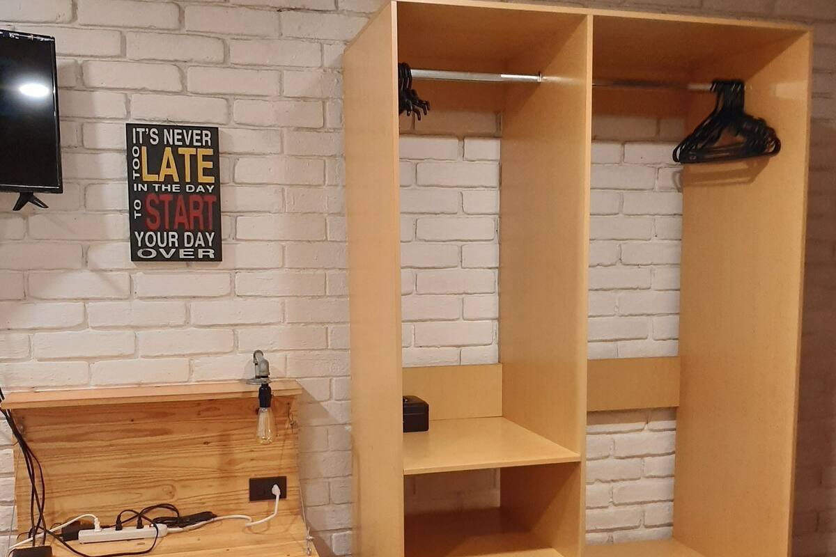 A room with a brick-patterned wall, a wooden desk with a chair, and a large open shelving unit.