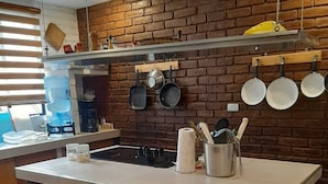 A kitchen with a brick wall, a central island with stools, hanging pots, and a water dispenser. - Tekla Dorms (Santa Tecla)