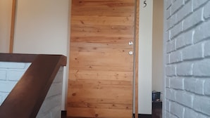 A hallway with a wooden door, a white brick wall, and a number '5' on the wall. - Tekla Dorms (Santa Tecla)