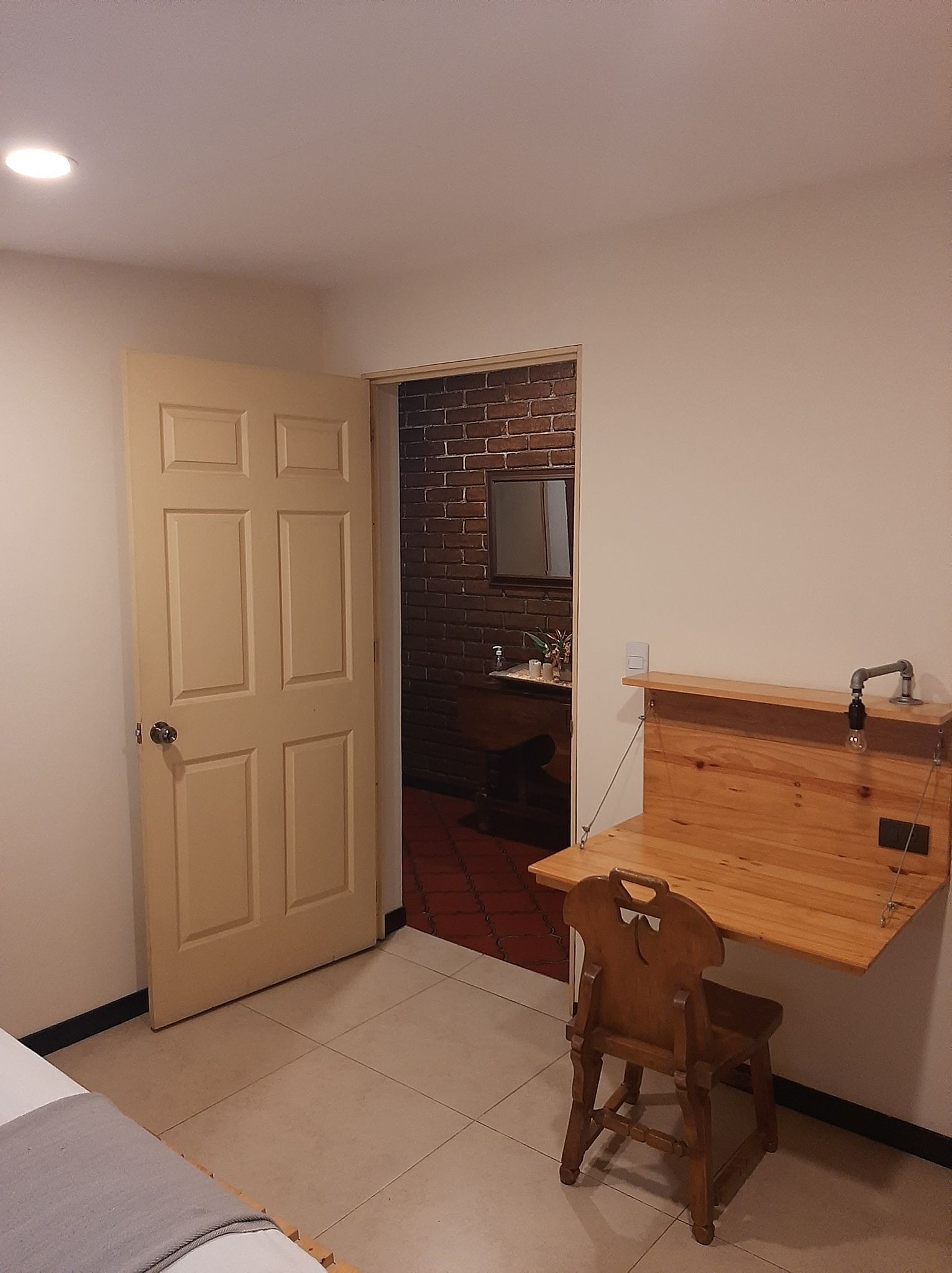 A small room with a wooden desk, a chair, a door, and a brick wall.