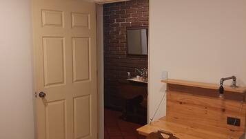 A small room with a wooden desk, a chair, a door, and a brick wall.