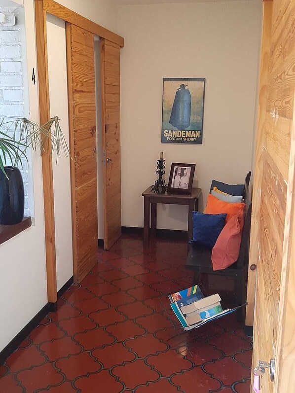 A hallway with a wooden door, a framed picture on a small table, and a poster on the wall. - Tekla Dorms (Santa Tecla)