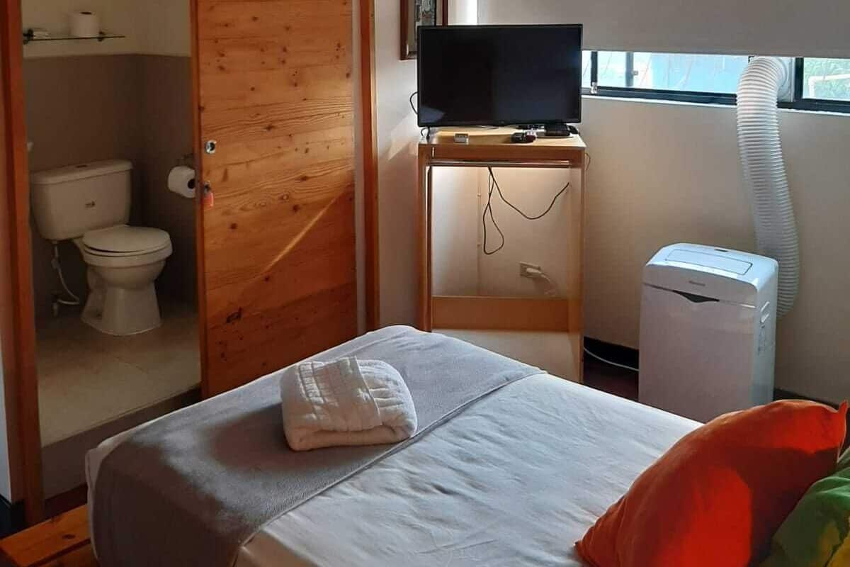 A bedroom with a bed, a television on a stand, a heater, and a window with blinds.