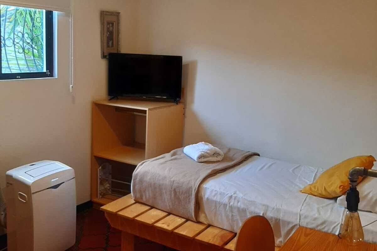 A small, compact room with a bed, a desk, a chair, a television, and a small heater.