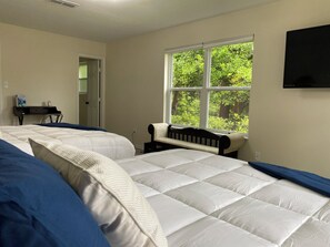 A bedroom with two beds, a desk, and a window with a view of trees.