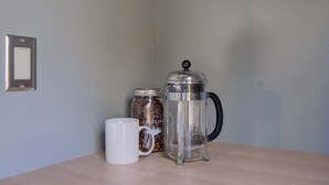 En kaffemaskine, en kaffekande og en hvid kop på et træbord foran en lys væg.