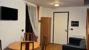 A room with a round wooden dining table, four chairs, a black sofa, a television mounted on the wall, and a door with a poster. - 1 Bed Flat - Sleeps 4 - Pets - Smoking on Terrace (Prague)