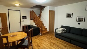 A living room with a wooden floor, a dining table with chairs, a staircase, and a dark-colored sofa. - 1 Bed Flat - Sleeps 4 - Pets - Smoking on Terrace (Prague)