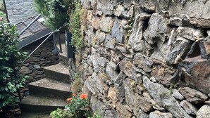 A stone wall with a flower bed and steps leading up to a door. - Come stay in our "Little Nest"! (Brissago)