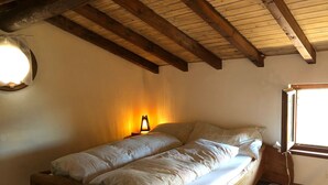 A single bed with a wooden frame in a room with a sloped ceiling and a window. - Come stay in our "Little Nest"! (Brissago)