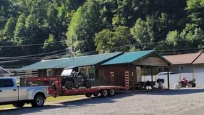 A truck with a trailer carrying a vehicle, parked in a gravel area with a building in the background. - The Mate Creek House, The Mate Creek House (Mingo County)