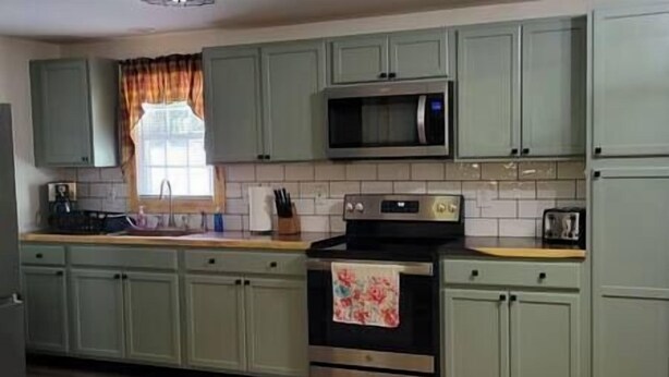 A kitchen with green cabinets, a microwave, an oven, and a window with curtains. - The Mate Creek House, The Mate Creek House (Mingo County)
