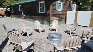 A wooden cabin with a porch area featuring Adirondack chairs and a metal barrel. - The Mate Creek House, The Mate Creek House (Mingo County)