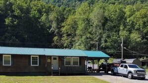 A single-story building with a green roof, a covered porch, and a truck parked in front. - The Mate Creek House, The Mate Creek House (Mingo County)
