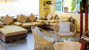 A room with a yellow wall, a ceiling fan, a sofa set, wicker chairs, and a window with a view of palm trees. - Luna lodge  (Olhuvelifushi)