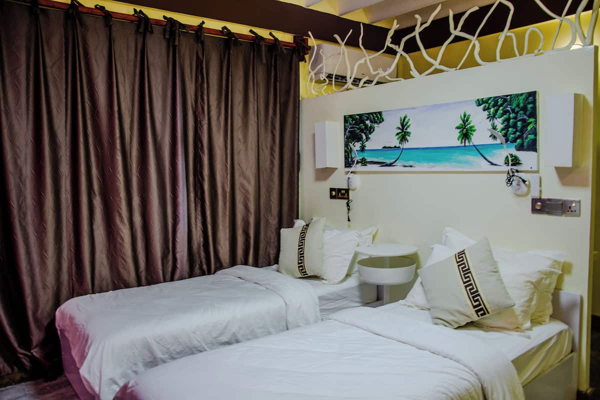 A hotel room with two beds, a painting of a beach scene, a bedside table, and a curtain.