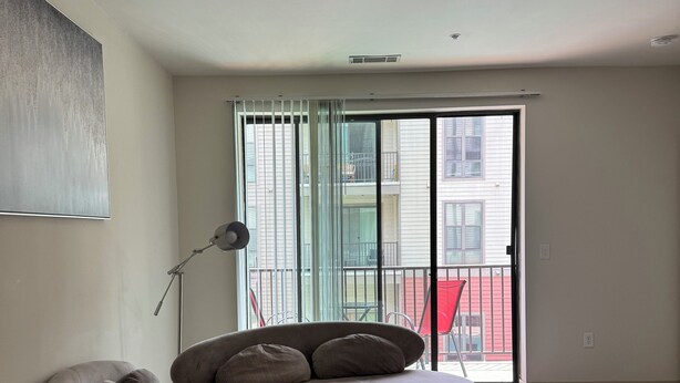 A modern living room with a curved sectional sofa, a floor lamp, and a large window with a view of a balcony. - Modern Downtown Apartment Near UAB (Birmingham)
