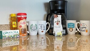 A kitchen counter with various coffee-related items, including mugs, a coffee maker, and coffee beans. - Modern Downtown Apartment Near UAB (Birmingham)