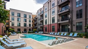 A pool area with lounge chairs and a swimming pool surrounded by multi-story buildings. - Modern Downtown Apartment Near UAB (Birmingham)