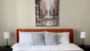 A hotel room with a large bed, a ceiling fan, and a cityscape painting on the wall. - Modern Downtown Apartment Near UAB (Birmingham)