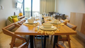 A dining table set for six with white plates, bowls, and glasses, surrounded by wooden chairs.