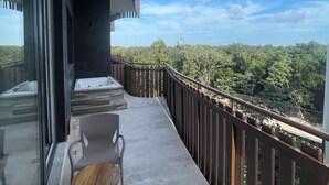 Un balcón con vistas a una zona boscosa, una mesa con sillas y un ventanal que da a un espacio interior.