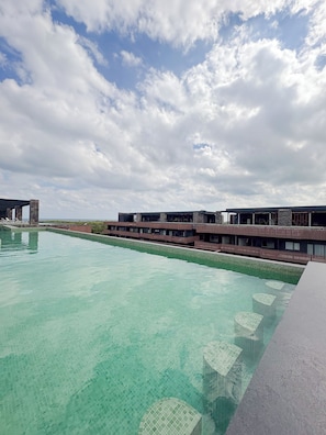 A large outdoor swimming pool with clear water, surrounded by a modern building with multiple balconies.
