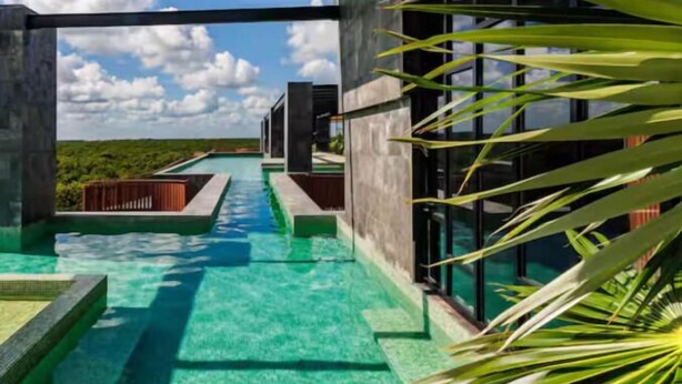 Una piscina infinita moderna con agua azul cristalina, rodeada de arquitectura contemporánea y vistas al cielo y las nubes.