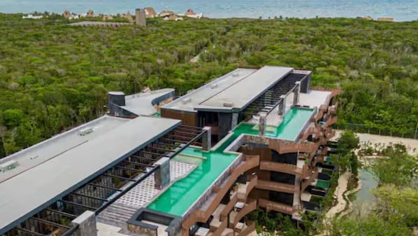 A modern hotel with a rooftop pool and a view of the surrounding greenery and coastline.