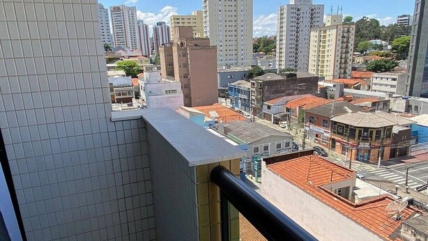 A balcony with a tiled floor and a view of a cityscape with various buildings. - Flat confortável próximo ao metrô (São Paulo)