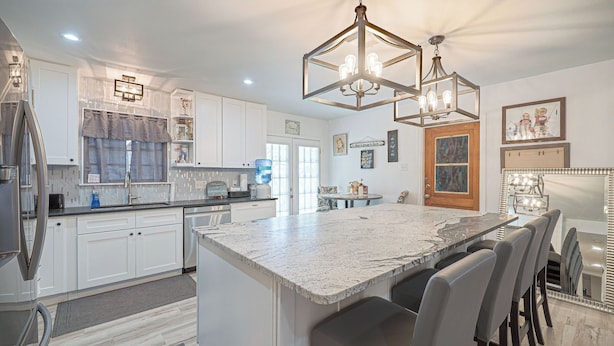 A modern kitchen with white cabinetry, a marble island, and a dining area with bar stools. - ALAMO CITY HOMESTYLE BEAUTY GREAT CENTRAL LOCATION, KIDDOS, & FURRY PET FRIENDLY (San Antonio)