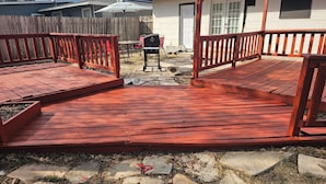 A wooden deck with a red railing, leading to a backyard with a barbecue grill and outdoor furniture. - ALAMO CITY HOMESTYLE BEAUTY GREAT CENTRAL LOCATION, KIDDOS, & FURRY PET FRIENDLY (San Antonio)