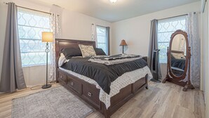 A bedroom with a large bed, a dresser, a mirror, and a floor lamp. - ALAMO CITY HOMESTYLE BEAUTY GREAT CENTRAL LOCATION, KIDDOS, & FURRY PET FRIENDLY (San Antonio)