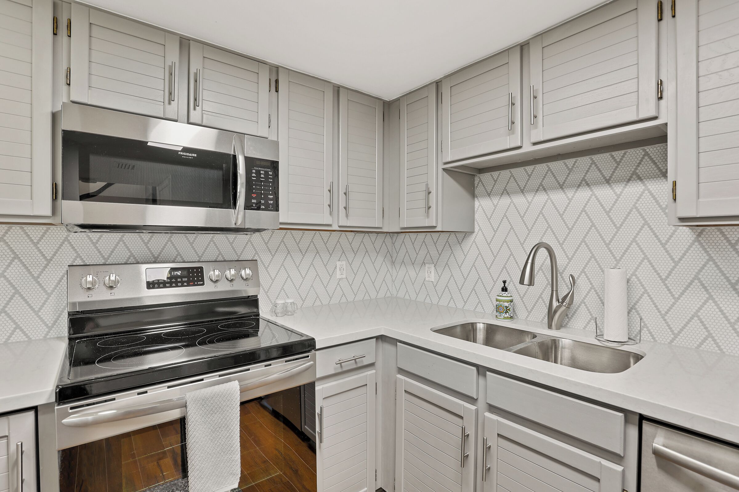 A kitchen with white cabinets, a stainless steel microwave, an oven, a sink, and a tiled backsplash.