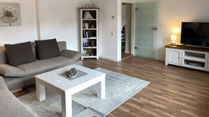 Un soggiorno con divano, tavolino, libreria, mobile TV e una porta che dà su un'altra stanza.
