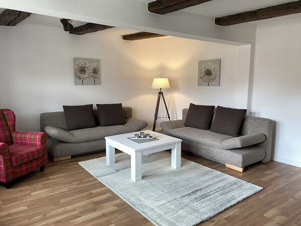 A modern living room with two grey sofas, a white coffee table, a red plaid armchair, and a floor lamp.