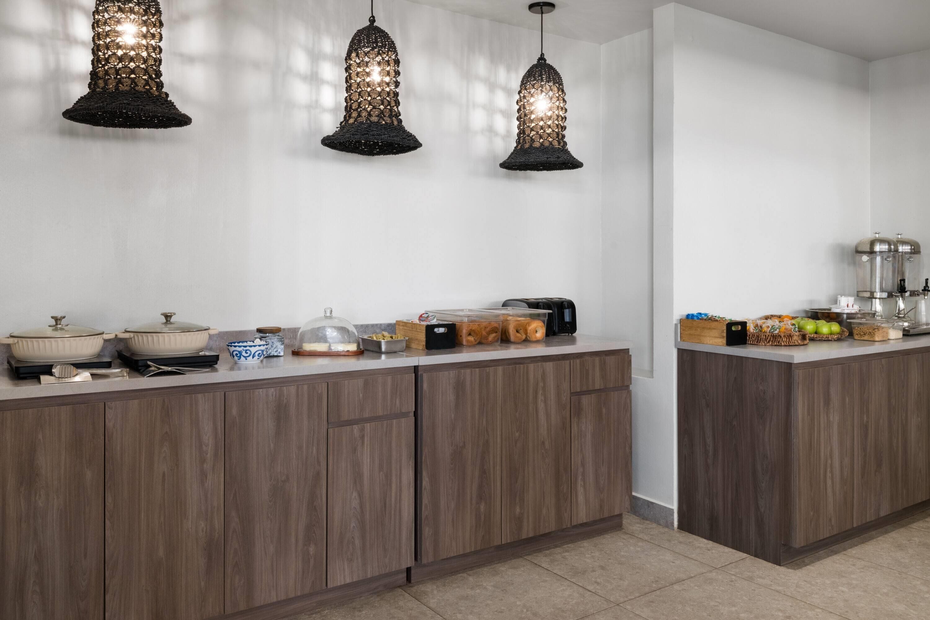 Uma cozinha moderna com armários de madeira, bancada com diversos utensílios de cozinha e três luminárias pendentes.