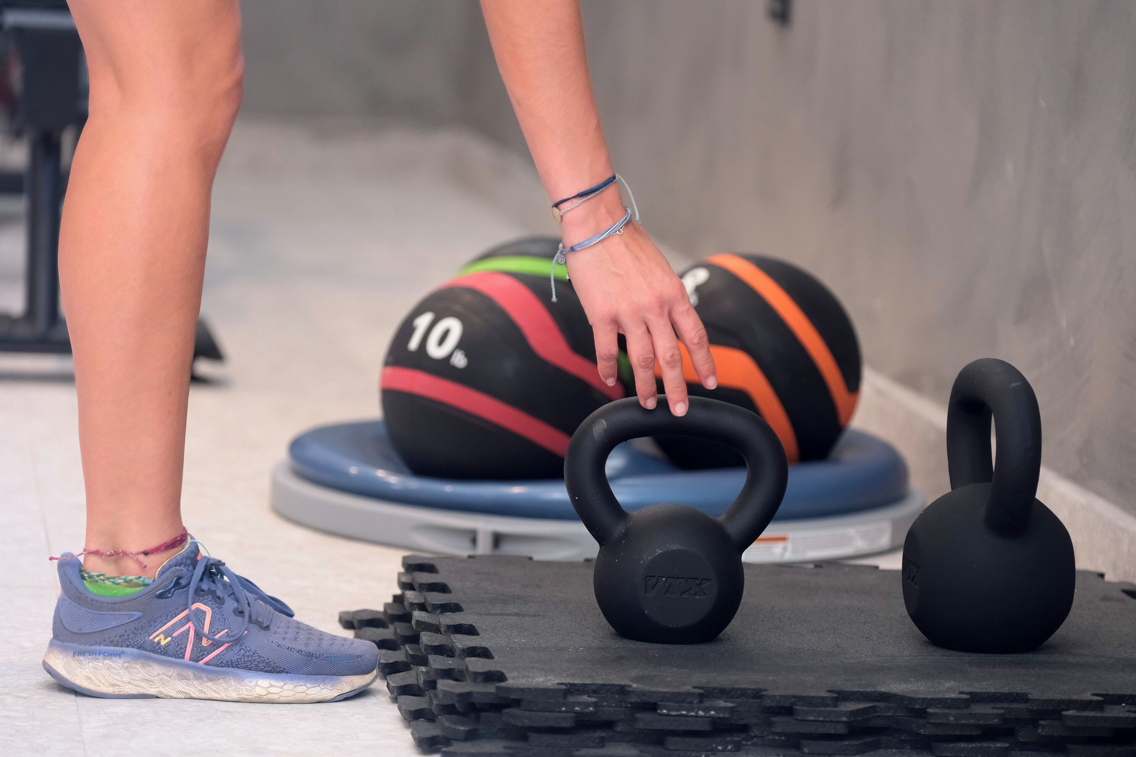 Een persoon staat naast een kettlebell en een medicine ball op een mat.