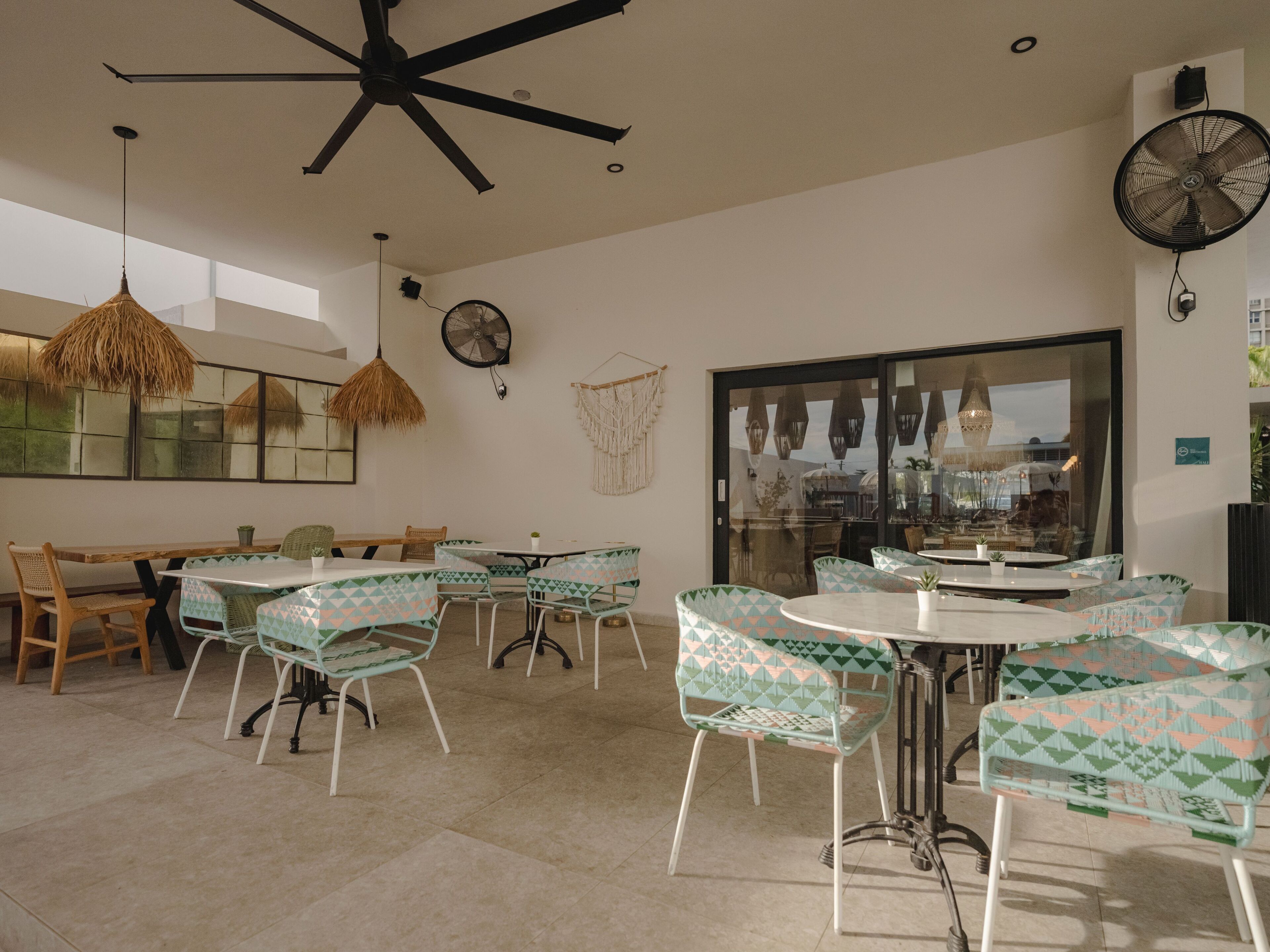 A spacious dining area with a high ceiling fan, a large window with a view, and a mix of wooden and metal chairs.