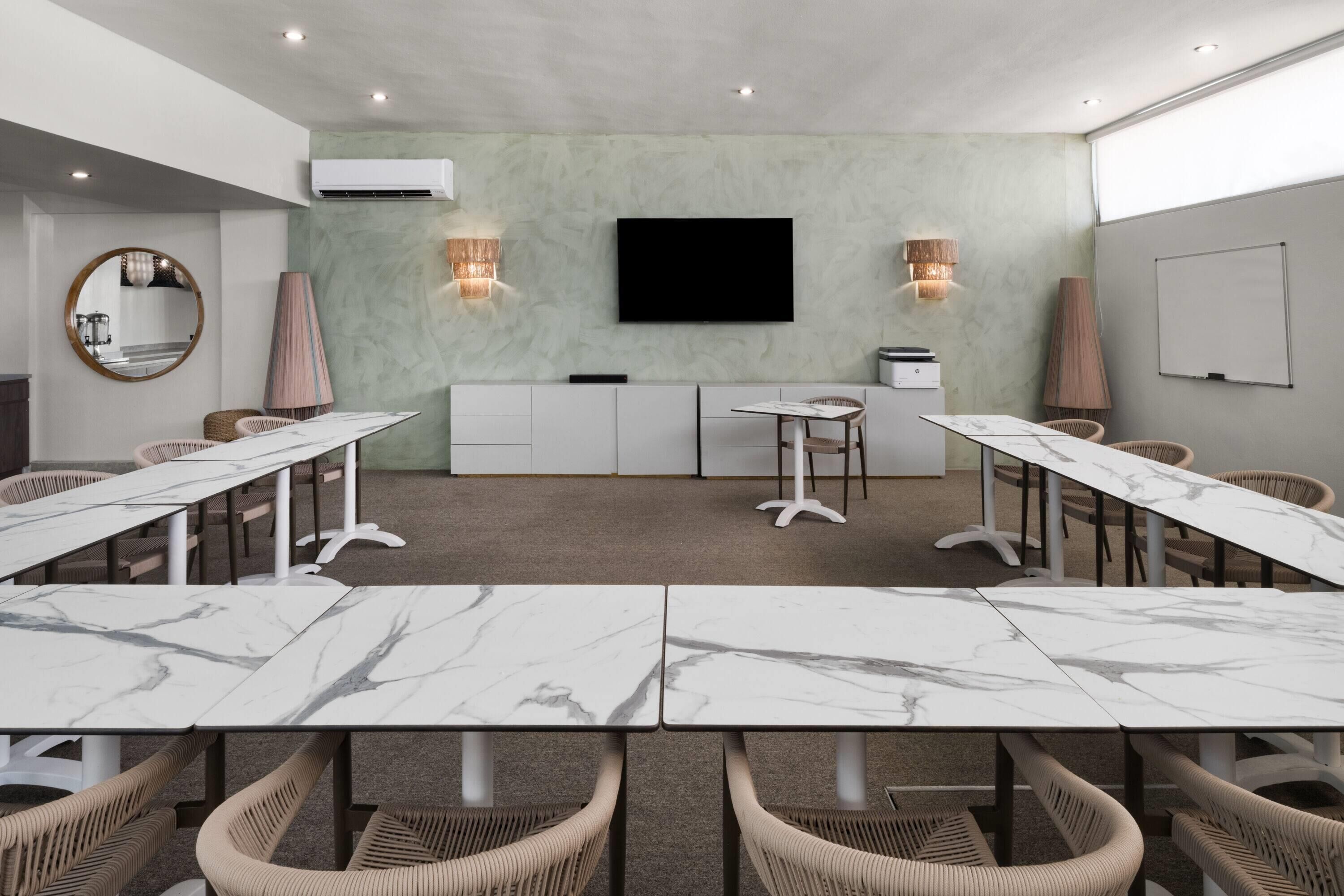 A conference room with marble tables, wicker chairs, a flat-screen TV, and wall-mounted sconces.