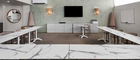 A conference room with marble tables, wicker chairs, a flat-screen TV, and wall-mounted sconces.
