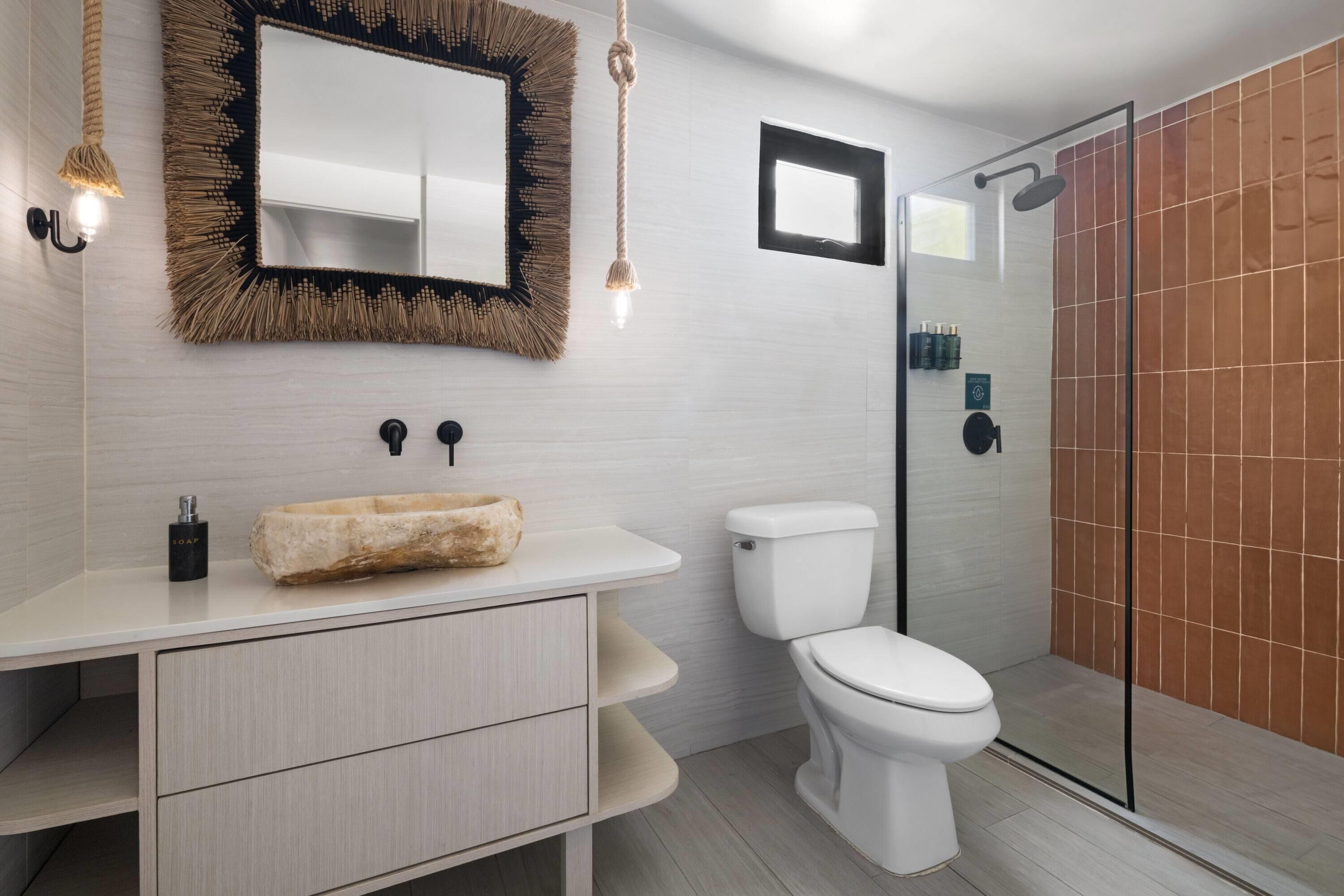 Un baño moderno con un lavamanos blanco, un inodoro, una cabina de ducha de vidrio y un espejo con marco texturizado.