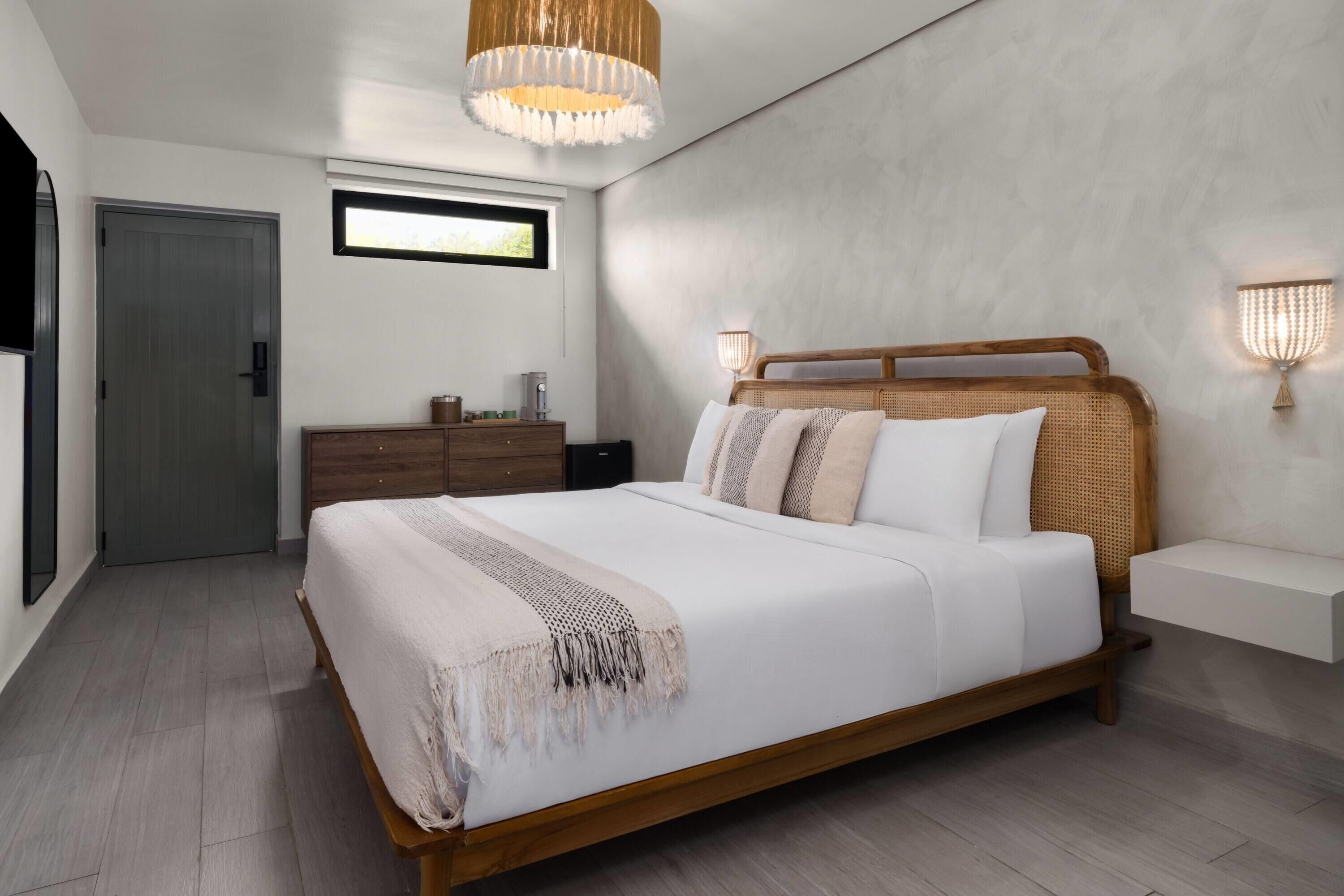 Un dormitorio moderno con una cama grande, cabecera de madera, lámparas de noche, una mesita de noche y una ventana con luz natural.