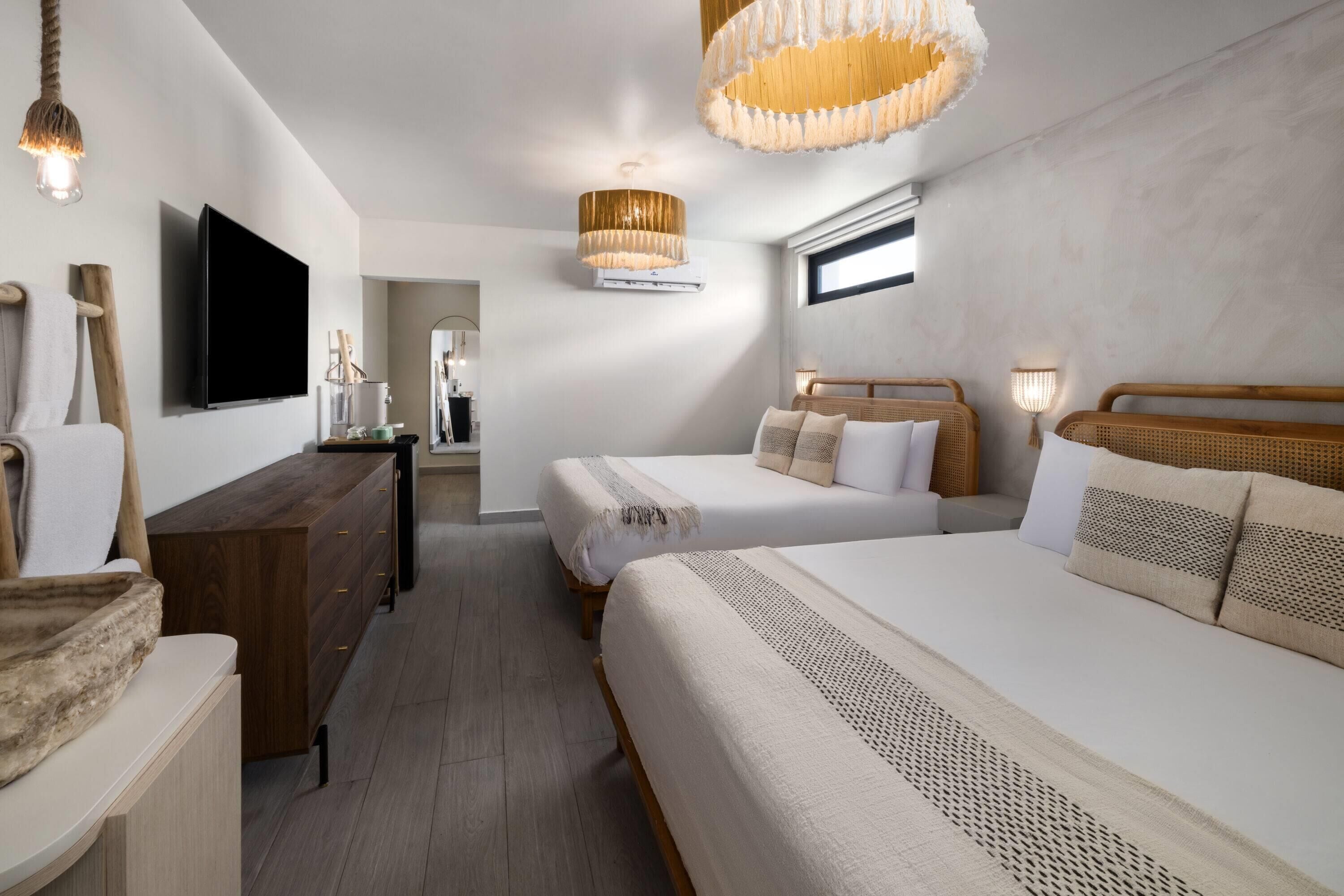 A modern hotel room with two beds, a TV, a wooden dresser, and a large window.